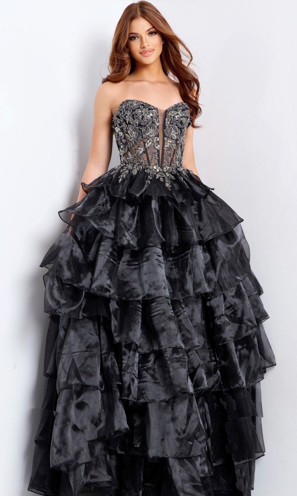 A woman poses in the Jovani 50259 Long Prom Dress, featuring a strapless black design with a tiered ruffled skirt and embroidered corset bodice, set against a plain light background.